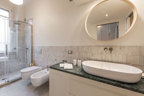 A modern bathroom with a large oval sink, a round mirror, a glass shower enclosure, and a toilet. - SEMPIONE, 51 – Spacious and bright (Milano)
