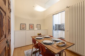 A dining area with a wooden table, chairs, and a view of the kitchen. - SEMPIONE, 51 – Spacious and bright (Milano)