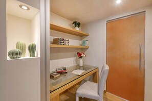 A room with a glass desk, a white chair, a wooden shelf with decorative items, and a sliding door.