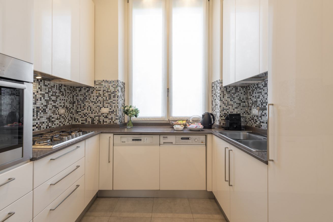 A compact kitchen with a dishwasher, a stove, and a window with curtains.