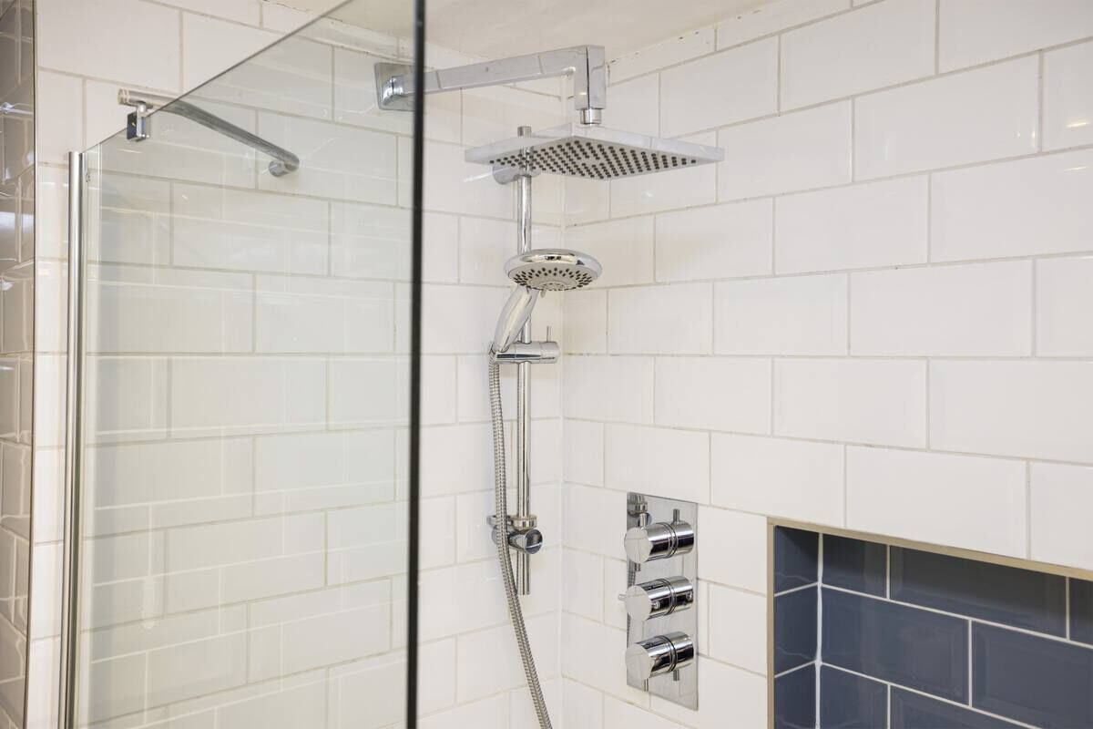 Ducha moderna con cabina de vidrio, accesorios cromados y pared de azulejos.