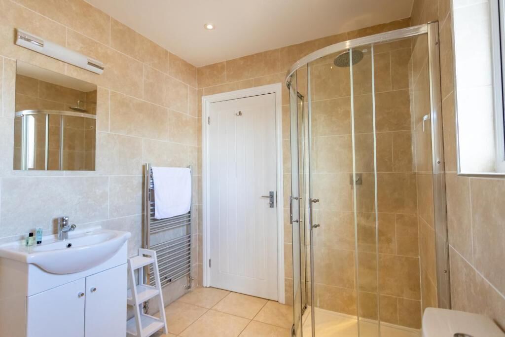 A modern bathroom with a glass shower enclosure, a white sink, and a mirror above it.