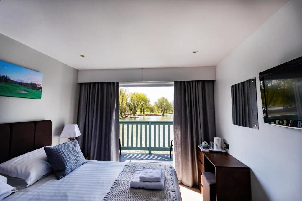 Ein Hotelzimmer mit Bett, Schreibtisch, Stuhl, Lampe und Blick auf eine grüne Terrasse und Bäume.