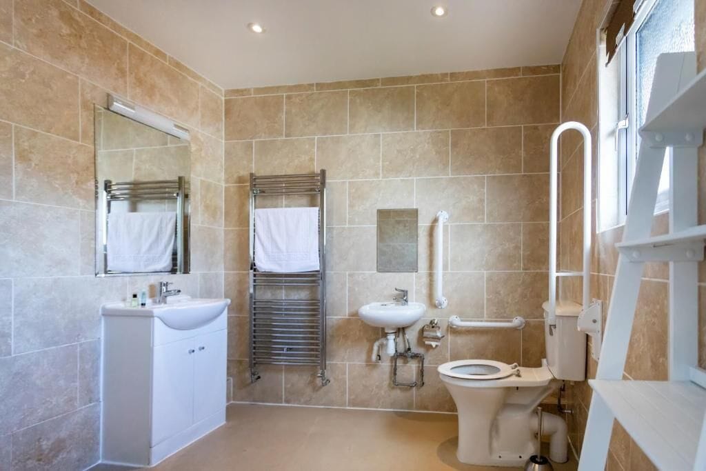 Un baño moderno con lavamanos, espejo, toallero, inodoro y zona de ducha.