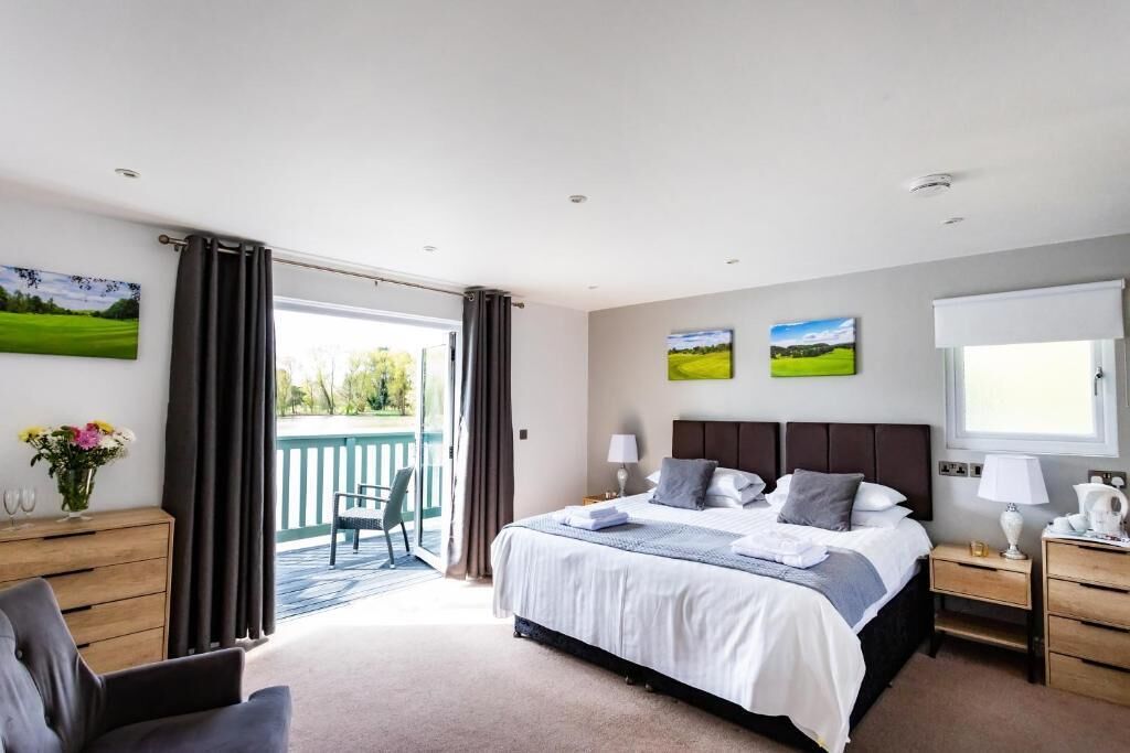 A bedroom with a large bed, a desk, a chair, and a balcony with a view of greenery.