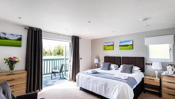 A bedroom with a large bed, a desk, a chair, and a balcony with a view of greenery.