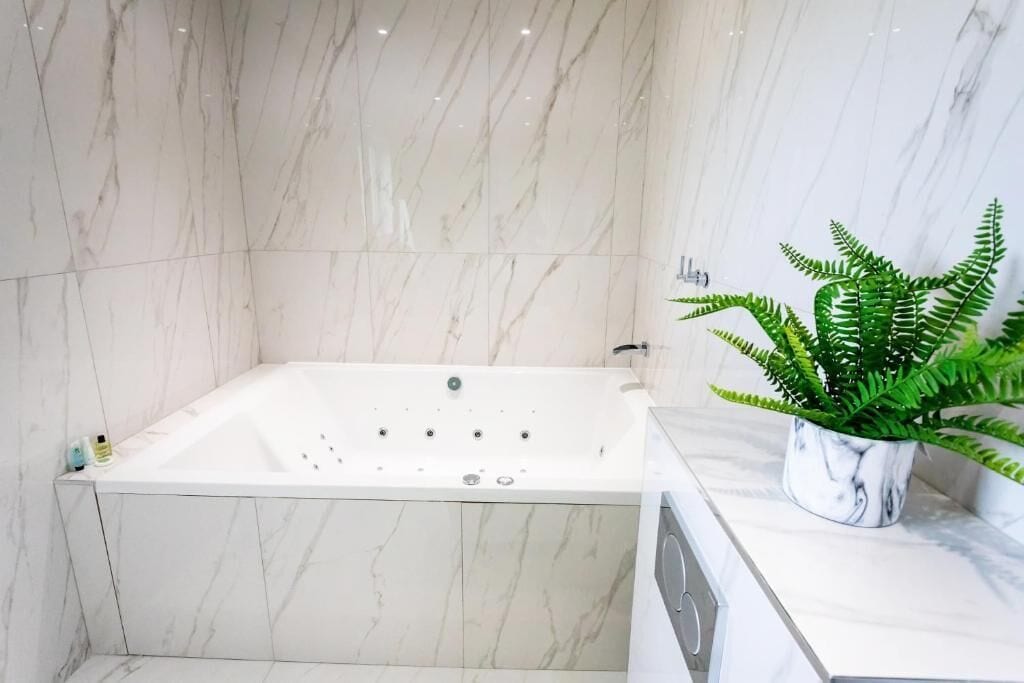 Un baño moderno con pared de mármol, una bañera independiente y un helecho en maceta sobre la encimera.