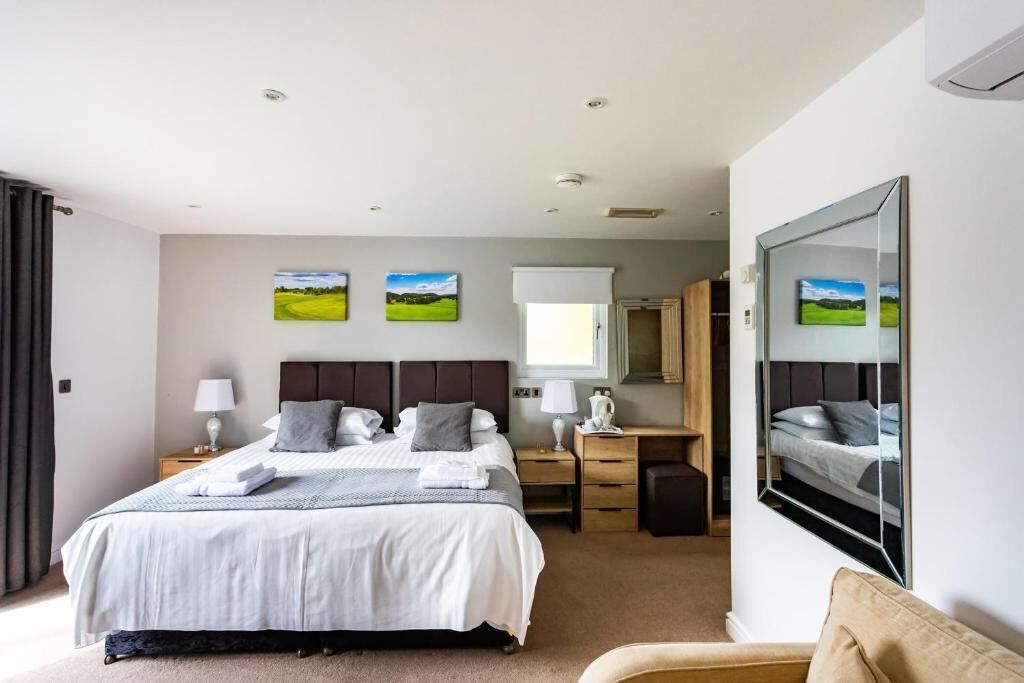 A modern hotel room with a large bed, bedside tables, a desk, and a mirror.