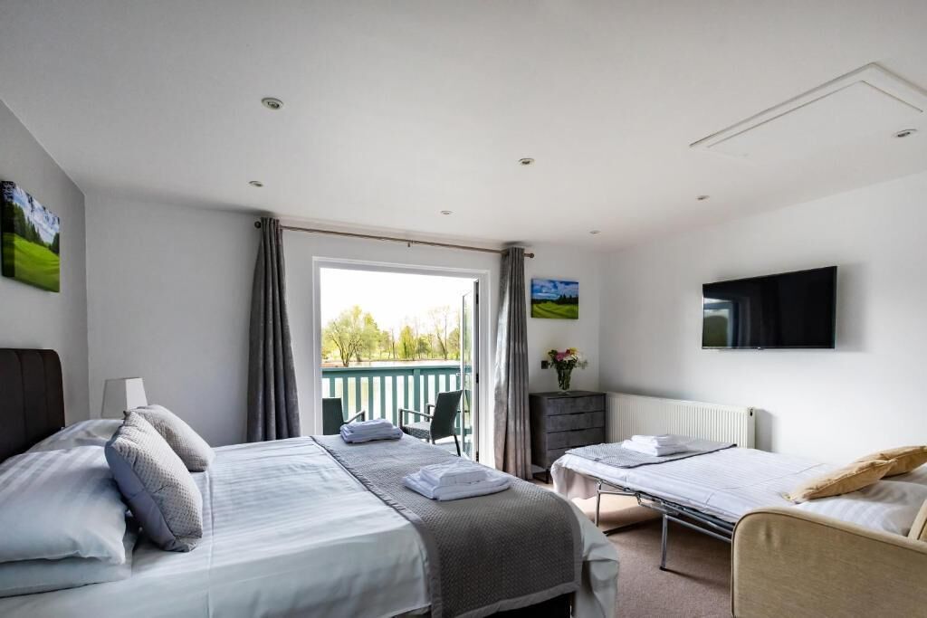Ein Hotelzimmer mit zwei Betten, einem Fernseher und einem Balkon mit Blick auf Grünflächen.
