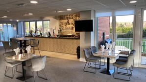 A restaurant with a bar area, seating arrangements, and a television screen. - The Vale Golf and Country Club (Pershore)