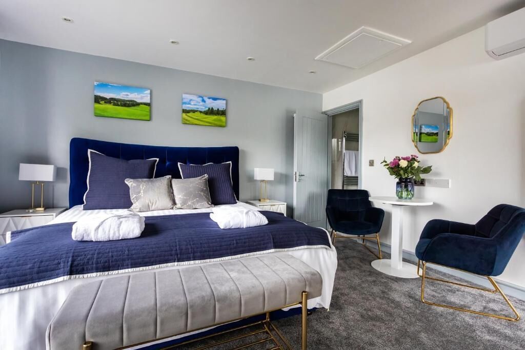 Une chambre d’hôtel moderne avec un grand lit, deux tables de chevet avec des lampes, une table ronde avec une chaise et un miroir au mur.