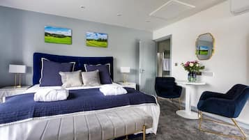 A modern hotel room with a large bed, two bedside tables with lamps, a round table with a chair, and a mirror on the wall.