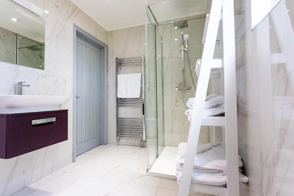 A modern bathroom with a glass-enclosed shower, a marble-tiled vanity, and neatly stacked towels.