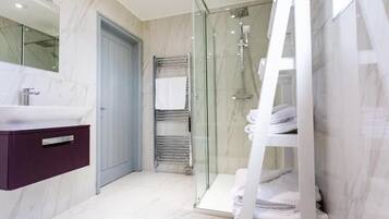 A modern bathroom with a glass-enclosed shower, a marble-tiled vanity, and neatly stacked towels.