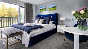 A bedroom with a large bed, a small table, a chair, and a view of the outdoors. - The Vale Golf and Country Club (Pershore)