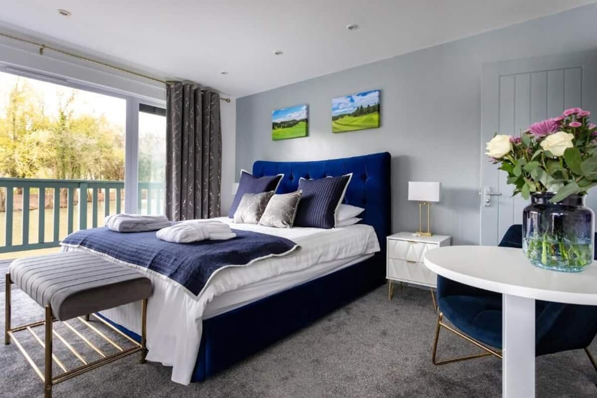 A bedroom with a large bed, a small table, a chair, and a view of the outdoors.