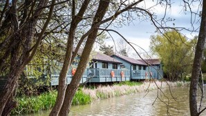 A houseboat with a blue exterior and a deck, surrounded by water and trees. - The Vale Golf and Country Club (Pershore)