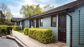 A row of light blue cabins with dark brown doors, a paved walkway, and neatly trimmed bushes.