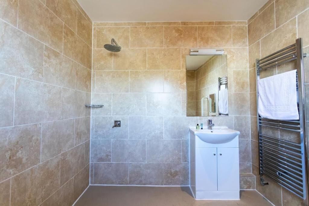 A bathroom with beige tiles, a white sink, a mirror, and a towel rack.