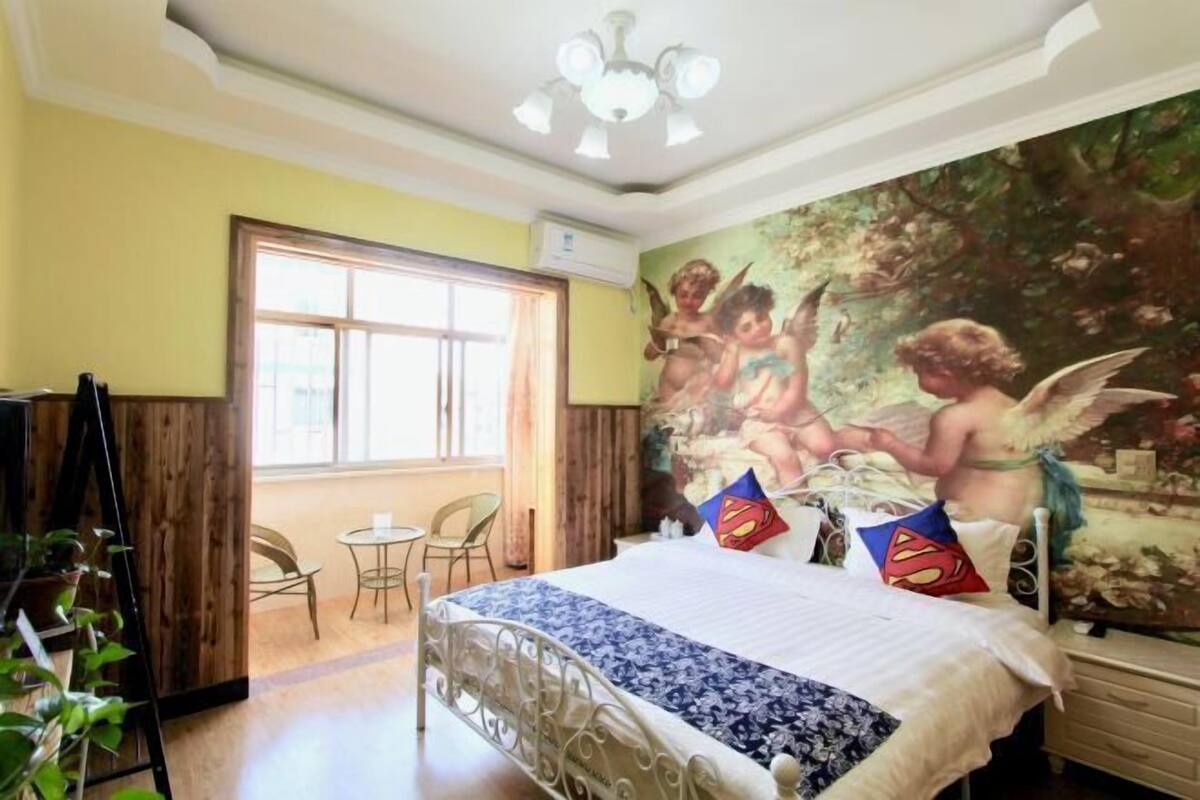 Un dormitori amb un llit, un mural, una finestra i un ventilador de sostre.