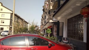Une voiture rouge est garée dans une rue résidentielle bordée d’immeubles à plusieurs étages, de balcons et d’une lanterne rouge.