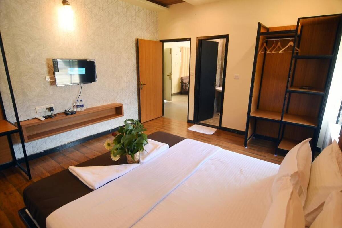 Une chambre d’hôtel comprenant un lit, un téléviseur fixé au mur, un banc en bois, un miroir et une armoire.