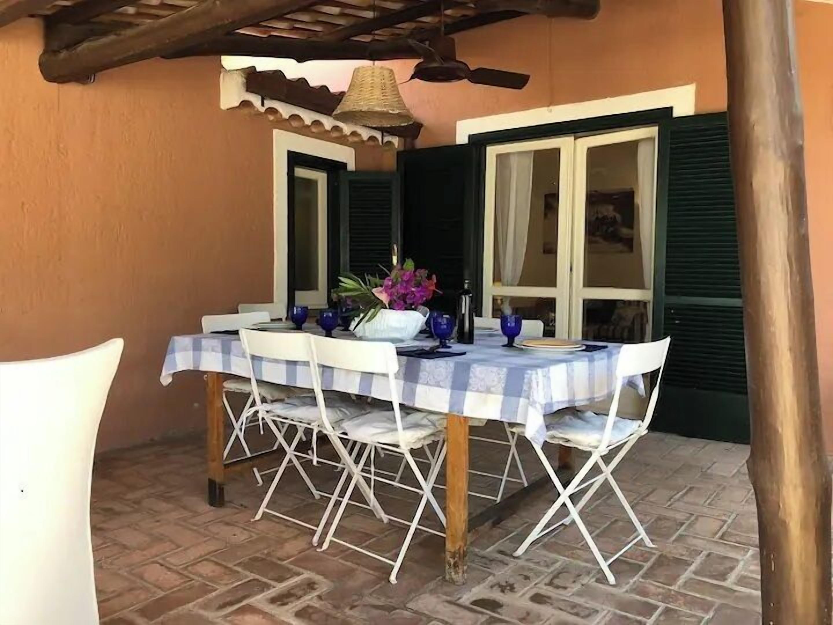 Un'area pranzo con tavolo imbandito per quattro persone, sedie bianche e tovaglia a quadretti blu e bianchi.