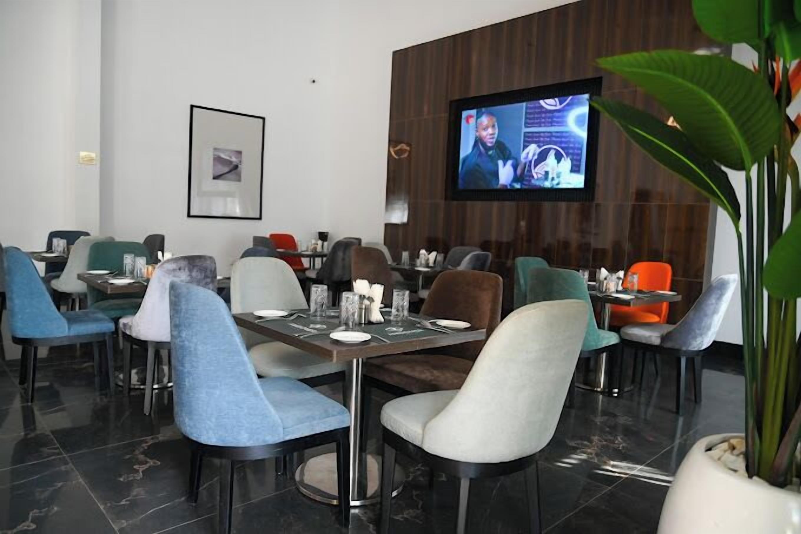 A modern dining area with multiple tables and chairs, a television screen, and a framed picture on the wall.