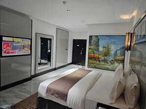 A modern hotel room with a large bed, a painting of a cityscape, a TV on the wall, and a door leading to another room. - The Andover Hotel  (Enugu)