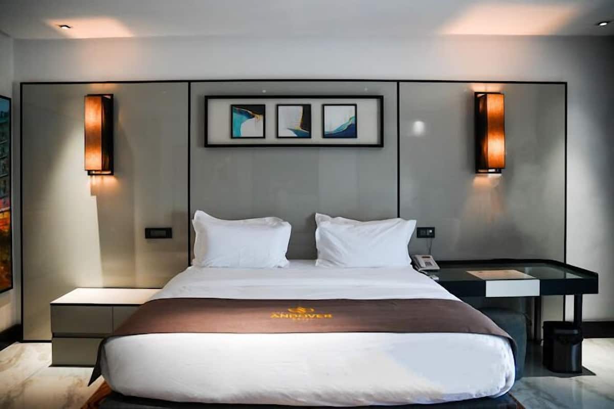 A modern hotel room with a large bed, two bedside tables, and a desk with a chair.