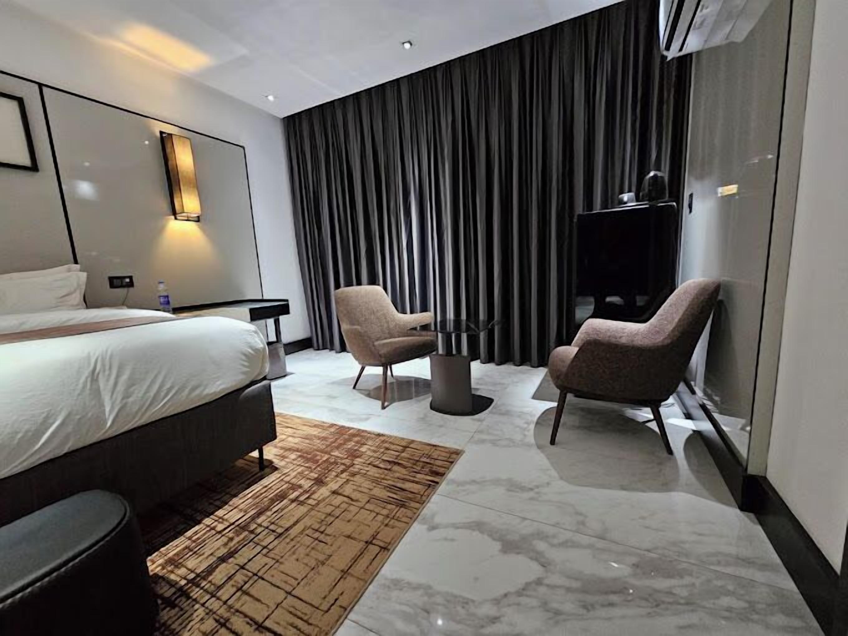 A modern hotel room with a large bed, two armchairs, a small table, and a TV.
