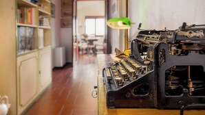 A vintage typewriter on a wooden table in a room with a tiled floor and a bookshelf filled with books. - Villa Pietraia (Certaldo)