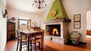 A dining area with a brick fireplace, wooden furniture, and a view through an open door. - Villa Pietraia (Certaldo)