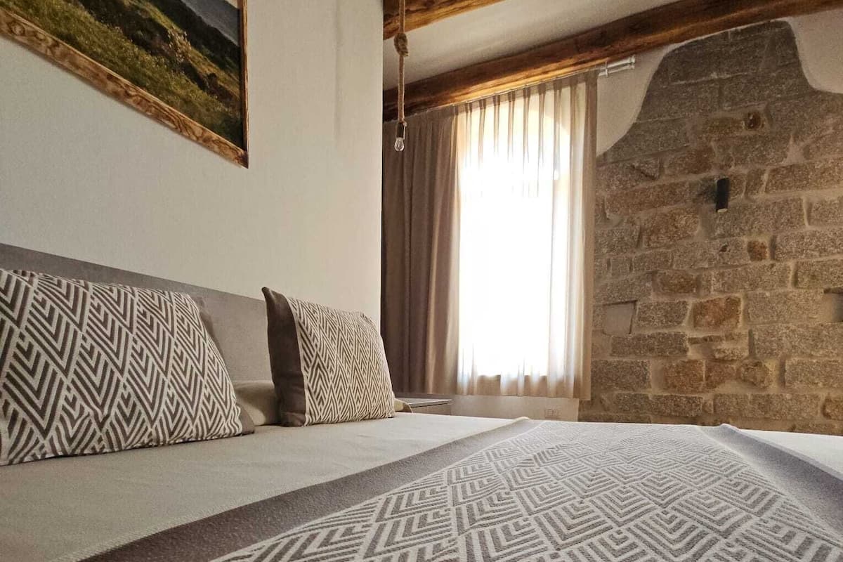 Ein Schlafzimmer mit einem großen Bett, gemusterten Kissen, einer Steinwand und einem Bild an der Wand.