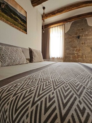 Ein Schlafzimmer mit einem großen Bett, gemusterten Kissen, einer Steinwand und einem Bild an der Wand.