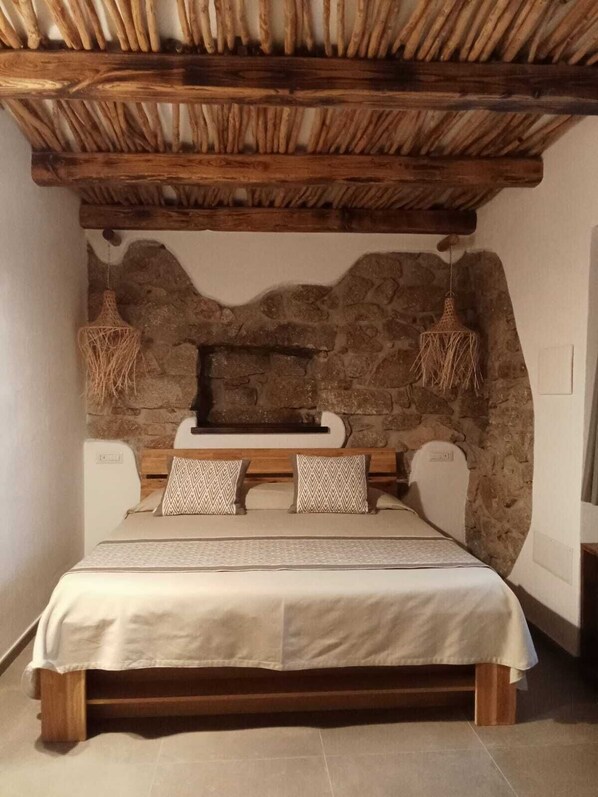 A bedroom with a stone wall, wooden bed frame, and two hanging light fixtures.