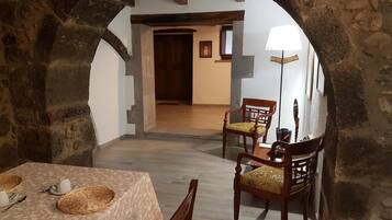 A dining area with stone arches, wooden chairs, a table with a tablecloth, and a lamp.
