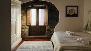Ein Schlafzimmer mit steinernen Rundbögen, Holzbalkendecke, einem Bett mit aufgerollten Handtüchern und einem gerahmten Bild an der Wand.