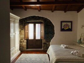Un dormitorio con un arco de piedra, vigas de madera en el techo, una cama con toallas enrolladas y un cuadro en la pared.
