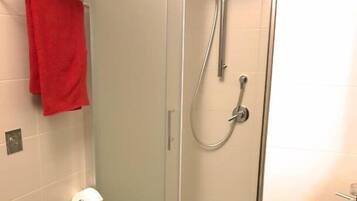 Un baño con ducha de vidrio, inodoro, lavamanos y una toalla roja en un estante.