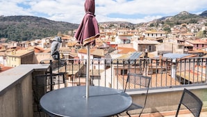 Ein Balkon mit rundem Tisch und Stühlen, mit Blick auf eine dicht bebauten Stadt mit Terrakotta-Dächern und einer gebirgigen Landschaft im Hintergrund.