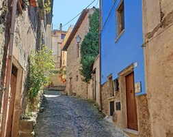 Una estrecha calle adoquinada bordeada por edificios con muros de piedra y un edificio de color azul.