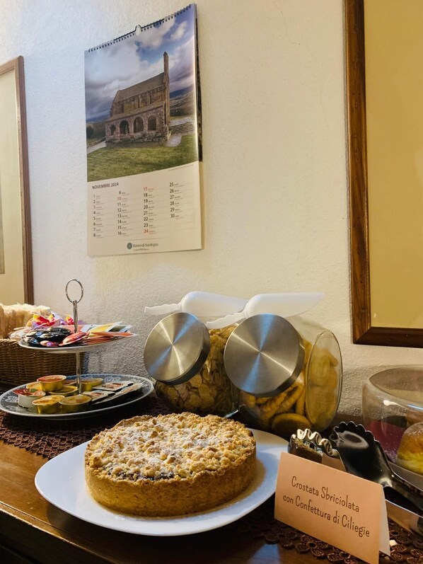 Una mesa de postres con un pastel que dice 'Crostata Sbriciolata con Confe' y un calendario en la pared.