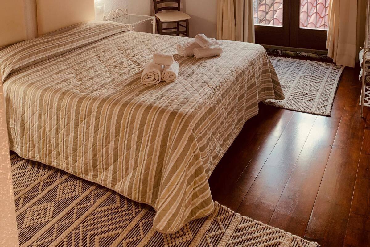 Un dormitorio con techo de madera, una cama con colcha a rayas, una silla, una mesita y un ventanal con cortinas.