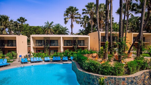 A hotel with a pool surrounded by palm trees and lounge chairs. - Bakadaji Hotel (Serrekunda)