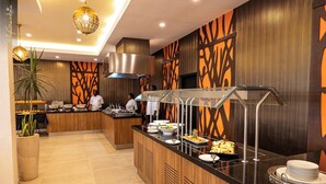 A modern hotel kitchen with a buffet setup, including a variety of dishes and a chef preparing food. - Bakadaji Hotel (Serrekunda)
