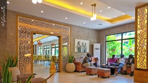 A lobby with a reception desk, seating area, and large windows with greenery outside. - Bakadaji Hotel (Serrekunda)