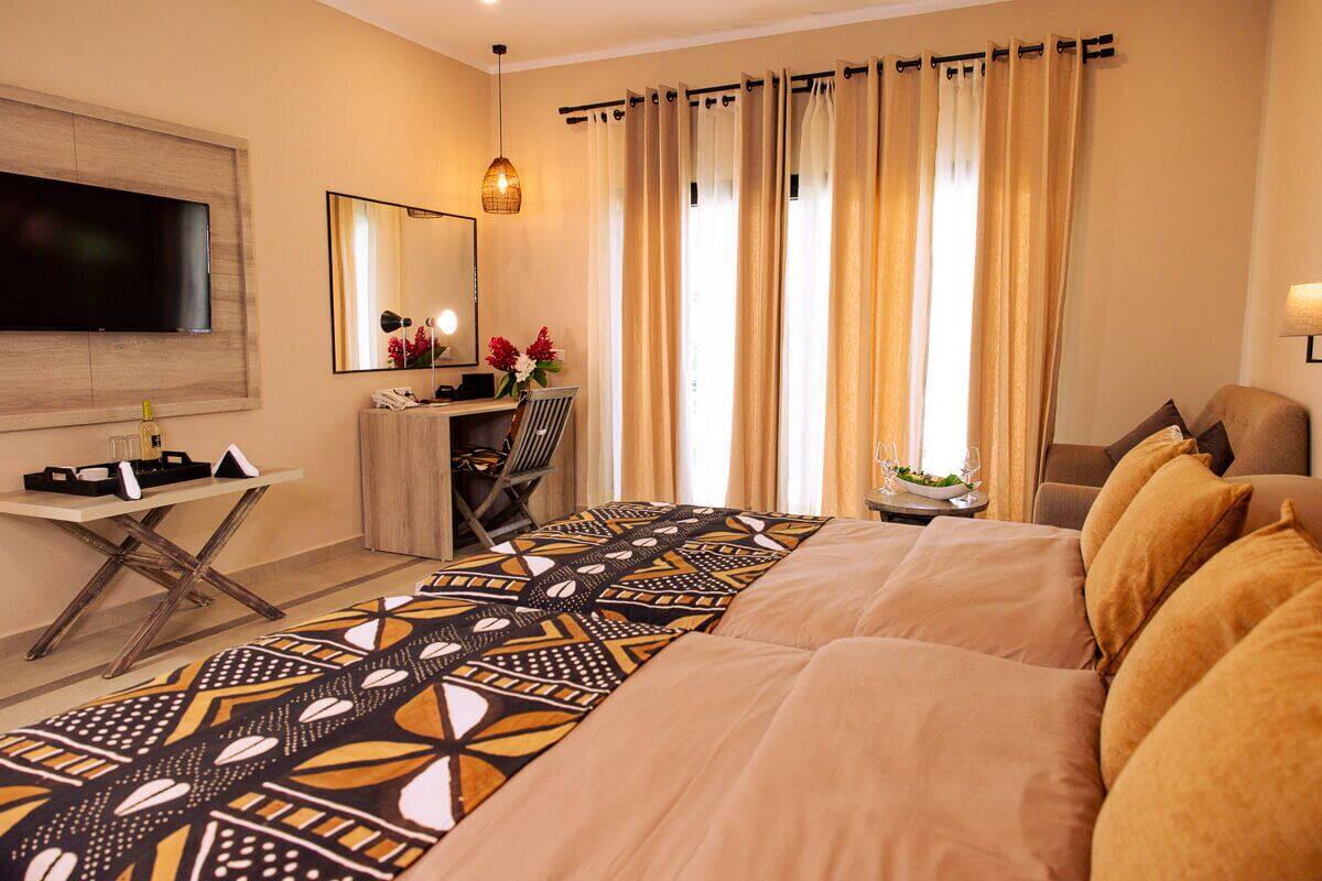 A hotel room with a large bed, a desk with a chair, a television, a mirror, and a window with curtains.