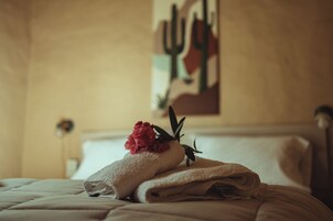 A neatly made bed with a folded towel and a red flower on top.