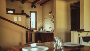 A dining area with a wooden table set for two, a kitchen in the background, and a window providing natural light. - Hacienda Altomonte (San Rafael)